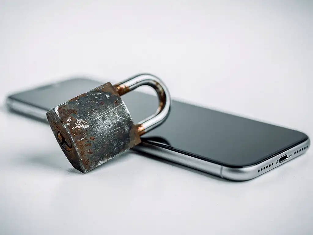 Rusted iron padlock clamped around a modern smartphone on a white desk, symbolizing mobile security and digital privacy.